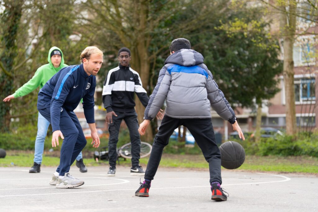 Jongens die buiten basketbal spelen met de buurtsportcoach